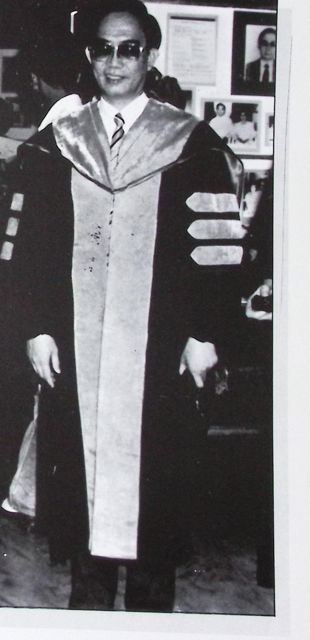 Full-length photograph of Chancellor Posadas in academic robes, smiling, in an office lined with framed photographs