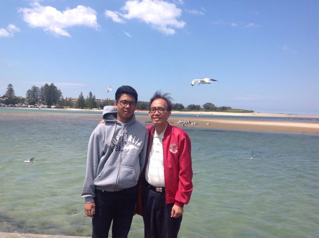 Gregor and Dad smiling by the water on a sunny day in Australia, gulls flying overhead