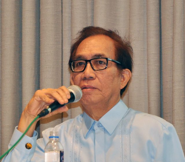 Roger Posadas in an embroidered barong, speaking into a microphone in front of a curtain