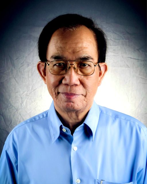 Portrait of Roger Posadas in his later years, in a light blue shirt and gold-rimmed glasses, against a gray backdrop