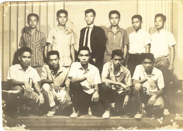 Old sepia group photograph of eleven teenage boys, six standing and five crouching in front; Roger is in the center of the front row