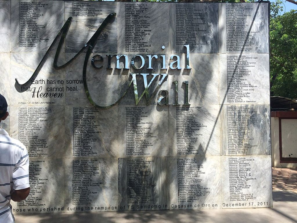 A stone memorial wall in a park, engraved with rows of names under the words Memorial Wall.