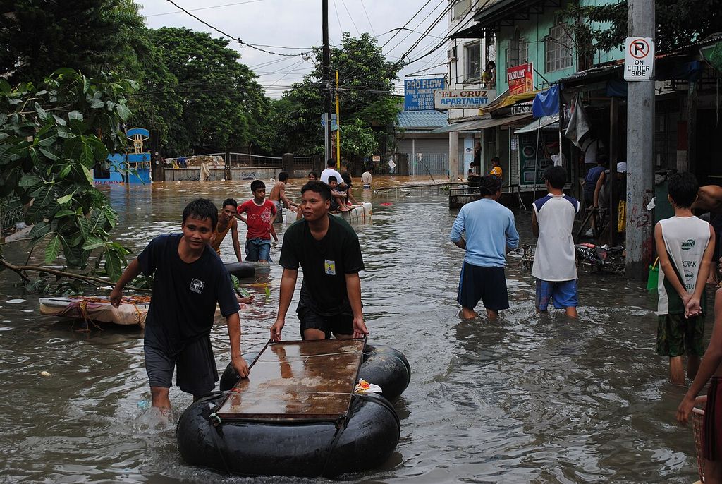 Men push a makeshift raft on an inner tube through a flooded street lined with shops.