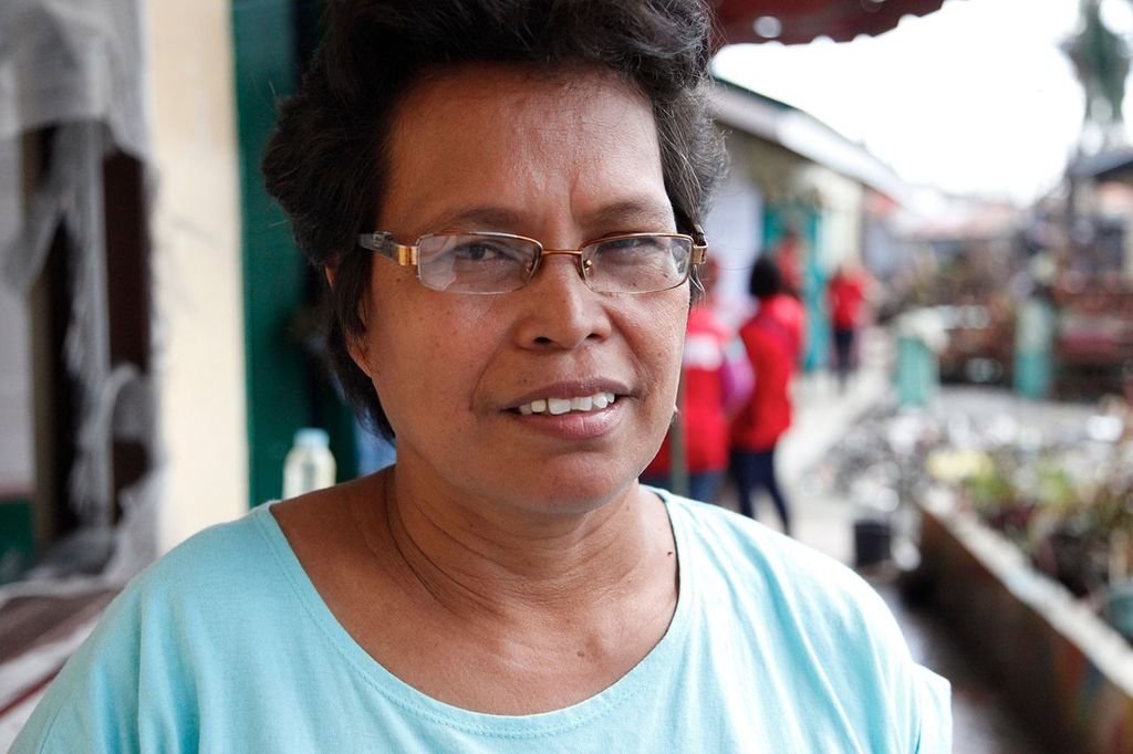 Portrait of a teacher in a light blue shirt standing in a damaged street.