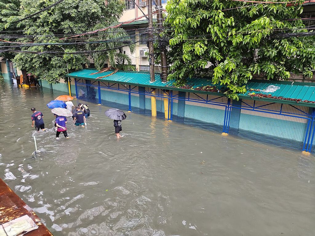 People with umbrellas wade through knee-deep floodwater along a street in Quiapo, Manila.